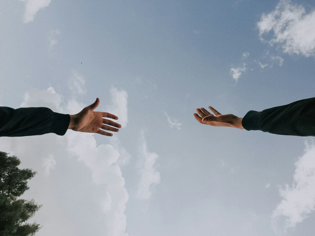 Two hands reaching toward each other against a cloudy sky